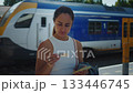 Passenger reviews ticket amidst travel routine, Woman verifies train ticket during busy station stop, Female traveler checks her ticket before boarding train at bustling station 133446745