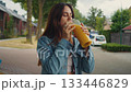 Woman savoring fresh citrus drink, Female individual relaxing with cold orange beverage outside, Young woman peacefully enjoying healthy citrus drink beneath leafy trees in suburban setting 133446829