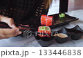 Woman using chopsticks picking up california roll served on black plate with pickled ginger, wasabi and soy sauce and mayonnaise sauce in small black bowls in a japanese restaurant 133446838