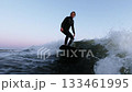 A Thrilling Surfing Adventure at Dusk: Mastering Waves and Balance on a Surfboard Amidst Calm Waters 133461995