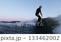 Dynamic Surfing Action at Dusk: A Surfer Riding the Waves with Precision and Thrill Against a Scenic 133462002
