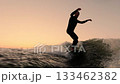 A Surfer Glides Through Waves at Sunset, Capturing the Thrill of Surfing and the Tranquil Beauty of 133462382