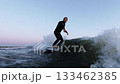 A Thrilling Surfing Experience Captured in Two Frames: An Athlete Riding Waves at Dusk in a Stylish 133462385