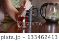 Woman stirring tea with spoon in glass at home, thoughtful moment closeup 133462413