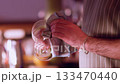 Barman occupation. Bar service. Man wiping glass in illuminated pub. Worker polishing glassware of alcoholic beverage with cloth in restaurant. 133470440