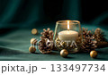 A glowing candle in a glass holder surrounded by pine cones and golden decor on a soft fabric, creating a warm festive atmosphere for winter celebration 133497734