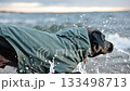 Black labrador enjoys splashing water at the beach in early evening light 133498713