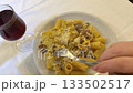 Pasta wine fork hand is seen reaching for a fork and knife to enjoy a plate of spaghetti. A glass of red wine sits nearby, creating a cozy atmosphere at home during an intimate dinner 133502517