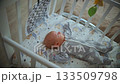 An infant lies in a crib and looks at a mobile that spins above its bed 133509798