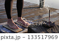 Woman Standing on Sadhu Board with Incense by Water 133517969
