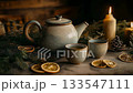 A rustic ceramic teapot and two cups on a festive Christmas table with burning candle, dried citrus fruit and evergreen branch 133547111