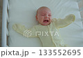 A one-month-old baby lies in a wooden crib, kicking and crying 133552695
