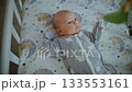 An infant lies in a crib and looks at a mobile that spins above its bed 133553161