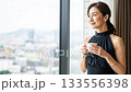 A Japanese woman in a black dress drinking coffee by the window in a hotel and smiling 133556398