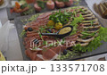 A stunning display of finely arranged meats, cheeses, and fresh greens captivates guests. Colorful garnishes and thoughtful presentation enhance the culinary experience at this elegant gathering. 133571708