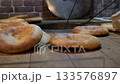 Close-up of a baker removing baked tortillas from a tandoor using special long hooks and serving it on the table. National Georgian bread. 133576897