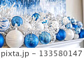 Festive holiday decorations with blue, white, and silver christmas baubles and snowy branches adorning a white mantelpiece. Elegant and sparkling ornaments creating a classic winter holiday mood 133580147