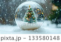 Festive glass snow globe containing a miniature decorated christmas tree with lights resting on fresh snow as snowflakes gently fall during a winter storm, creating a magical holiday atmosphere 133580148