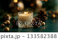 A glowing candle in a glass holder surrounded by pine cones and golden decor on a soft fabric, creating a warm festive atmosphere for winter celebration 133582388