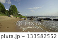 Sandy coastline of the Baltic Sea in Latvia. Yellow sand and large stones on the shore. Waves run onto the beach on a sunny day. Latvia, Gulf of Riga.  133582552