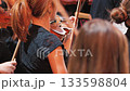 Close-up of musicians playing violins in an orchestra. The focus is on the back of a woman in a black lace top, surrounded by fellow musicians 133598804