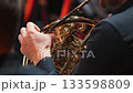Close-up of the French horn playing. The musician's hand presses the keys of a brass French horn, displaying intricate valves and tubes. The brass section of the orchestra 133598809