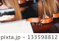 Close-up view of a violin in an orchestra setting, with blurred musicians in the background. The focus highlights the violin's polished wood and elegant curves 133598812