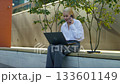 Smiling businesswoman multitasking with phone and laptop outdoors 133601149