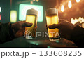Two hands holding glasses of beer, making a celebratory toast in a dimly lit bar, enjoying a refreshing drink during a social gathering and happy hour 133608235