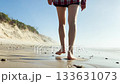 Close up of a woman walking barefoot on sandy beach near rocks and dunes. Steps in wet sand. Summer vacation, relaxation, freedom, seaside lifestyle, and nature journey 133631073