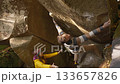 strong adult male climber climbs on overhanging boulder by it edges using wide hands grips, woman belay him. climbing outdoor in autumn forest. healthy active lifestyle, training outdoors. 133657826