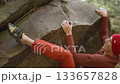 man rock climber climbs up on top of bouldering on edge of overhanging cliff. man reaching holds on slope rock surface. healthy lifestyle, active leisure. rock climbing outdoor in autumn forest. 133657828