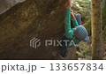 strong female climber climbs hard crag bouldering reaching holds on cliff edge showing strength and power of her fingers and forearms. healthy active leisure, rock climbing outdoors in autumn forest. 133657834