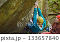 slow motion rock climbing outdoors in autumn forest. friends rock climbers climbs bouldering belaying each other. man in bright blue hoodie and yellow knitted cap hanging on edge of overhanging cliff 133657840