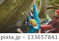 slow motion rock climbing outdoors in autumn forest. friends rock climbers climbs bouldering belaying each other. man in bright blue hoodie and yellow knitted cap hanging on edge of overhanging cliff 133657841