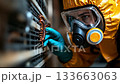 A man in a yellow hazmat suit and gas mask working on an air conditioner 133663063