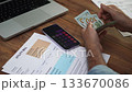 Old man surrounded by laptop and utility bills carefully counts dollar bills at table in office, male entrepreneur preparing cash to cover household expenses slow motion 133670086