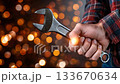 Hand holding a wrench against a blurred background of glowing lights in a workshop setting 133670634
