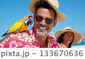 Man enjoys sunny beach day with colorful parrot while a woman relaxes in background 133670636