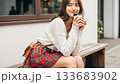 Smiling young Japanese woman drinking coffee on an outdoor bench 133683902