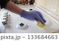 Person is cleaning a stove top with a yellow sponge 133684663