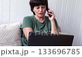 Woman engaging in phone conversation while typing on laptop in home setting 133696785