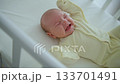 A one-month-old baby is lying in a white wooden crib, wearing a yellow onesie, kicking its legs and crying 133701491