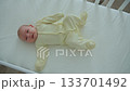 A one-month-old baby is lying in a white wooden crib, wearing a yellow onesie, kicking its legs and crying 133701492