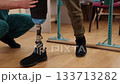 therapist guidance, prosthetic mobility, walking therapy. In well-lit rehab center, therapist assists prosthetic leg patient during walking practice. 133713282