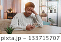 Young Indian man texting on smartphone while resting head on hand at table in living room at home 133715707