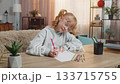 Young girl arranging colored pencils on table and drawing picture, admiring result with satisfaction 133715755