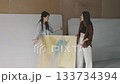 Two women discuss art creation while preparing a large canvas in a bright studio setting Two women discuss art creation while preparing a large canvas in a bright studio setting 133734394