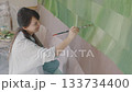 A woman paints a large green mural on a wall in a bright art studio, showcasing her creativity and talent A woman paints a large green mural on a wall in a bright art studio, showcasing her creativity and talent 133734400