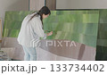Woman painting a large abstract art piece with green hues in a well-lit studio Woman painting a large abstract art piece with green hues in a well-lit studio 133734402
